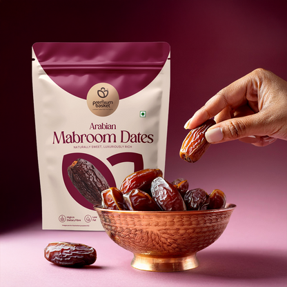 Hand holding date fruit with Arabian Mabroom Dates pouch and bowl
