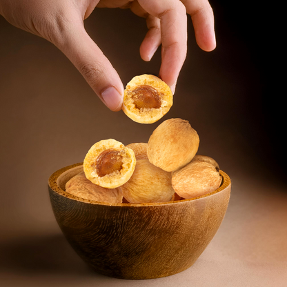 Hand picking a halved dried apricot from a wooden bowl of apricots