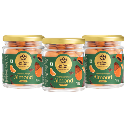 Three glass jars of orange-flavored almond snacks, gold lids, green labels
